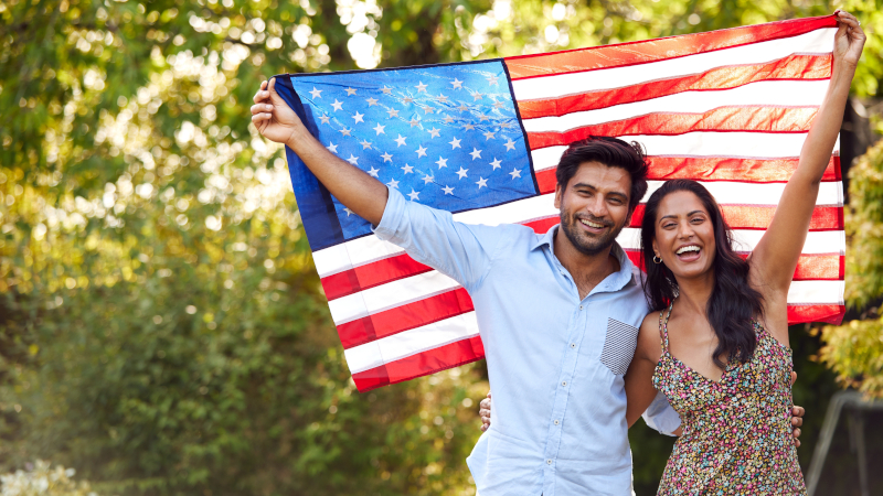 Joyful couple holding an American flag outdoors - Go For Desi